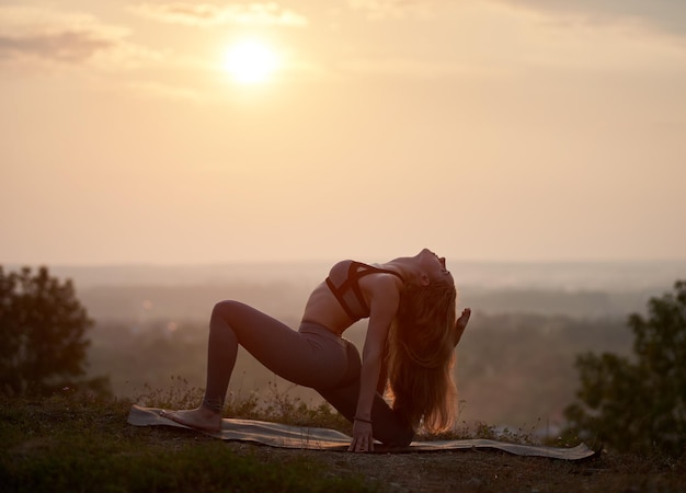 Giovane donna che fa esercizi di yoga all'aperto al tramonto