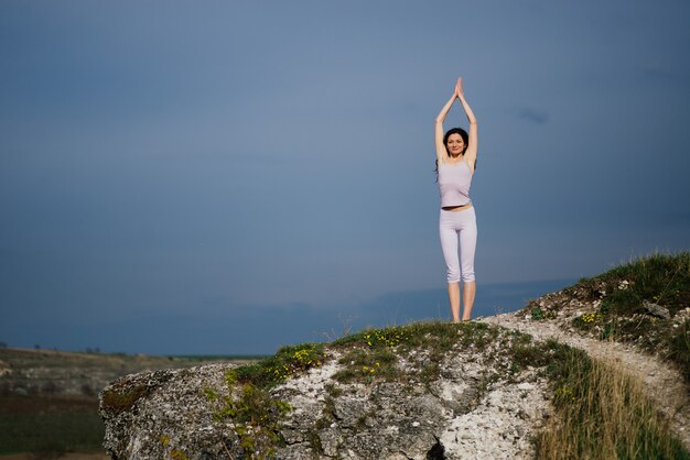 Giovane donna che fa esercizio complesso di yoga su una roccia