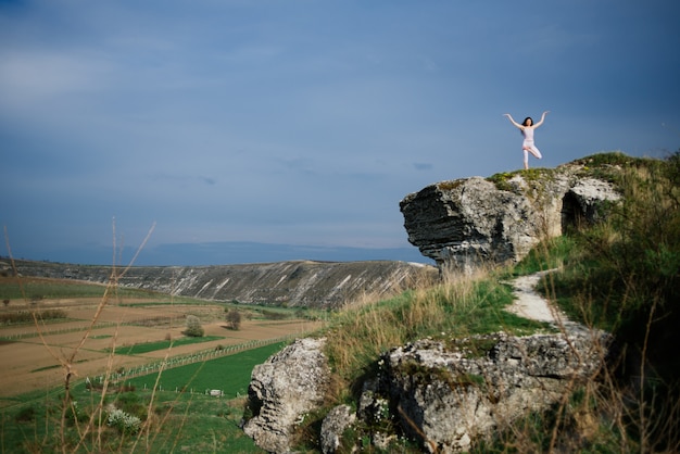 Giovane donna che fa esercizio complesso di yoga su una roccia