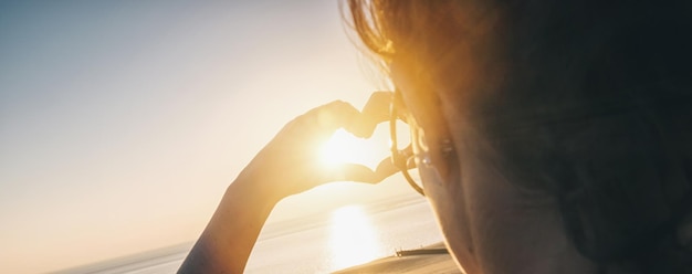 Giovane donna che fa il cuore con le mani al tramonto sull'oceano