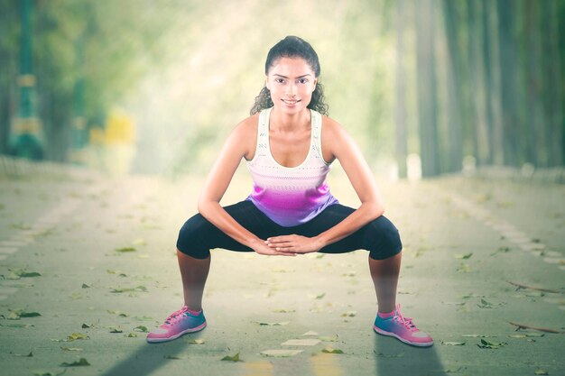 Giovane donna che fa il riscaldamento prima di fare jogging al parco mentre sorride alla macchina fotografica e indossa abiti sportivi