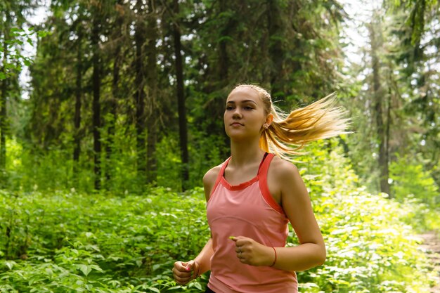 Giovane donna che fa jogging attraverso una foresta soleggiata