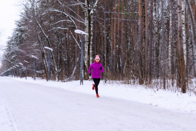 Giovane donna che fa jogging su un vicolo innevato in una giornata invernale