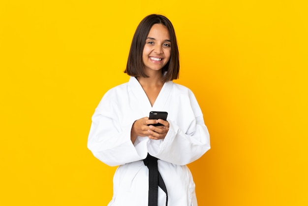 Giovane donna che fa karate isolata su superficie gialla che invia un messaggio con il cellulare