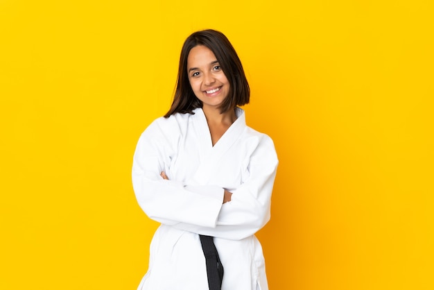 Giovane donna che fa karate isolato su sfondo giallo con le braccia incrociate e guardando avanti