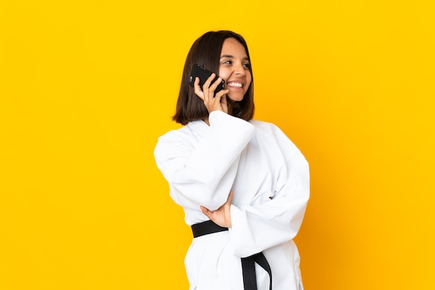 Giovane donna che fa karate isolato sulla parete gialla che tiene caffè da portare via e un cellulare