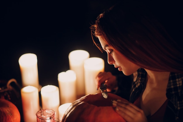 Giovane donna che fa la zucca di Halloween Jack-o-lantern con candele al buio. Mani femminili che tagliano le zucche con il coltello