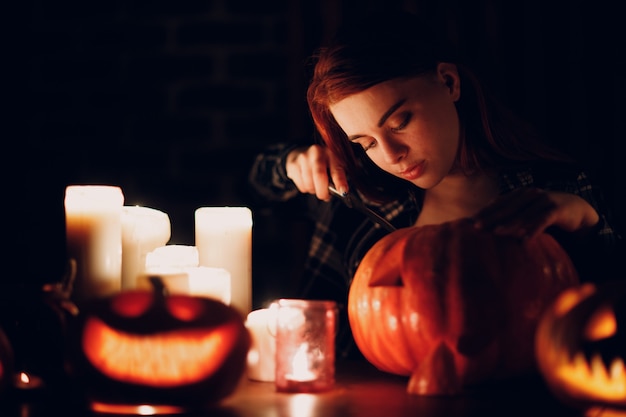 Giovane donna che fa la zucca di Halloween Jack-o-lantern. Mani femminili che tagliano zucche con coltello.