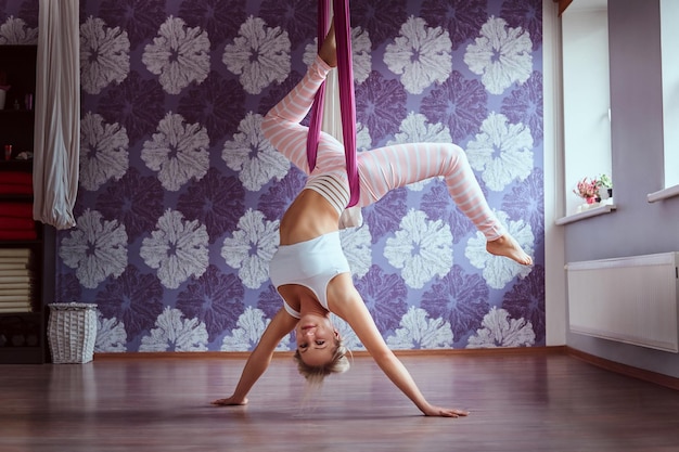 Giovane donna che fa pratica yoga aerea in amaca viola nel fitness club.