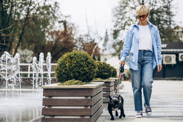 Giovane donna che fa una passeggiata con il suo bulldog francese dell'animale domestico