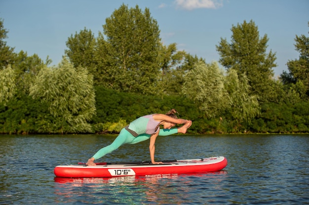 Giovane donna che fa yoga a bordo sup con paddle yoga posa vista laterale concetto di armonia con la natura