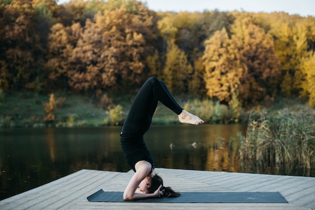 Giovane donna che fa yoga asana in natura vicino al lago