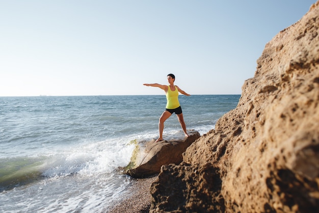 Giovane donna che fa yoga in riva al mare. Posa del guerriero.