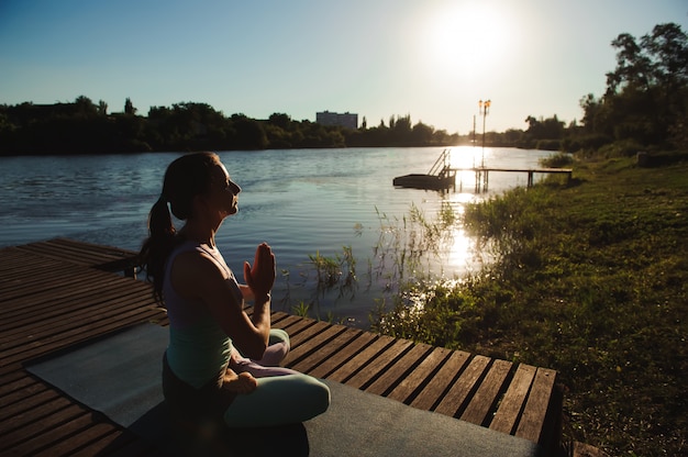 Giovane donna che fa yoga nel parco di mattina vicino al lago.