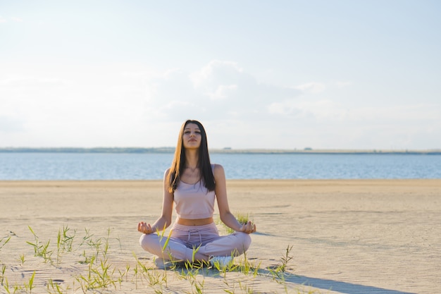 Giovane donna che fa yoga sulla spiaggia