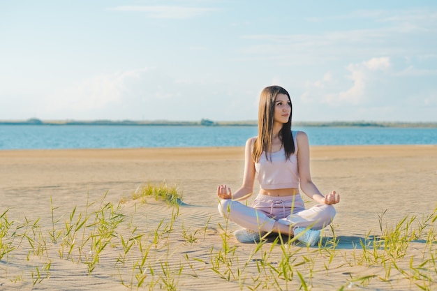 Giovane donna che fa yoga sulla spiaggia