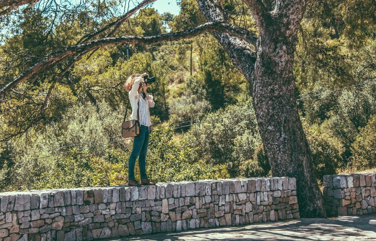 Foto giovane donna che fotografa su un muro di pietra contro la foresta