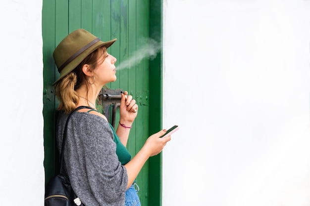 Giovane donna che fuma sigaretta elettronica appoggiata su una vecchia porta