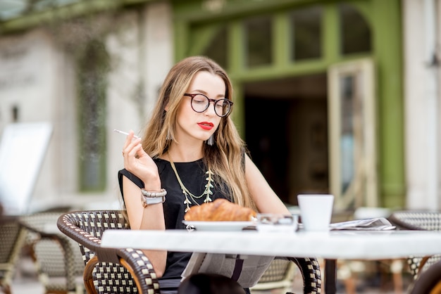 Giovane donna che fuma una sigaretta mentre fa colazione all'aperto nella tipica terrazza del caffè francese in Francia