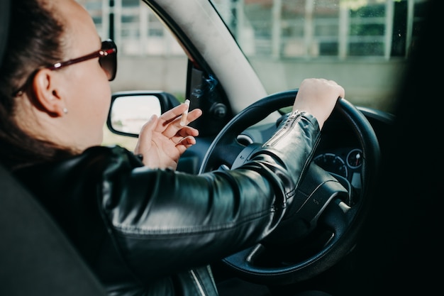 Giovane donna che fuma una sigaretta mentre si guida un'auto, concetto di trasporto