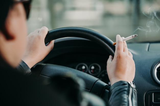 Giovane donna che fuma una sigaretta mentre si guida un'auto, concetto di trasporto