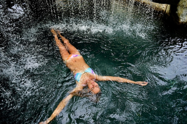 Giovane donna che galleggia in acqua in piscina con cascata