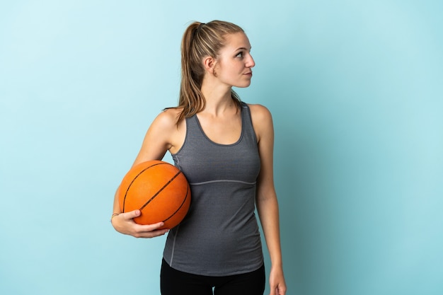 Giovane donna che gioca a basket isolato su blu guardando al lato