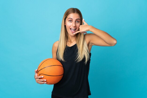 Giovane donna che gioca a basket isolato sul muro bianco che fa il gesto del telefono. Richiamami segno