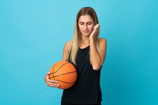 Giovane donna che gioca a basket isolato sul muro bianco frustrato e che copre le orecchie