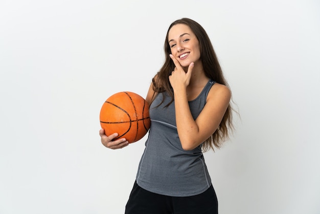 Giovane donna che gioca a basket sopra la parete bianca isolata felice e sorridente