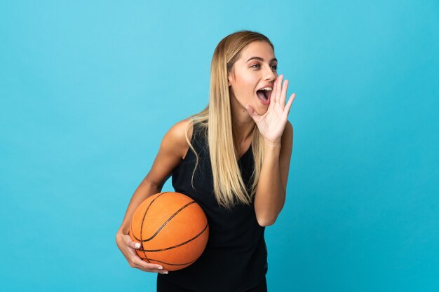 Giovane donna che gioca a basket su bianco gridando con la bocca spalancata di lato