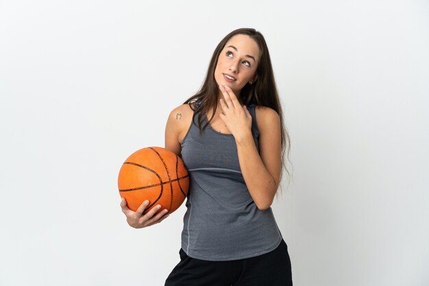 Giovane donna che gioca a basket su sfondo bianco isolato guardando in alto mentre sorride