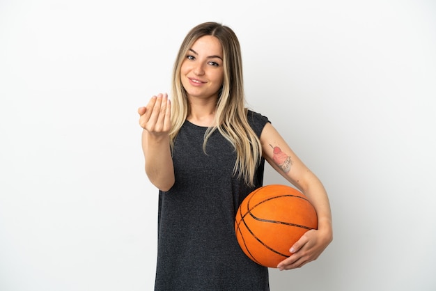 Giovane donna che gioca a basket su un muro bianco isolato che invita a venire con la mano. Felice che tu sia venuto