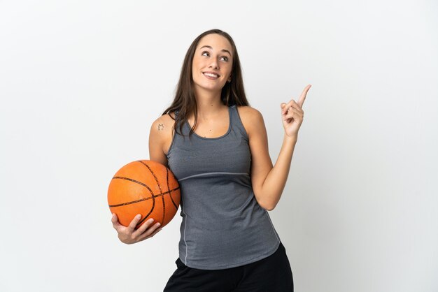 Giovane donna che gioca a basket sul muro bianco isolato rivolto verso l'alto una grande idea