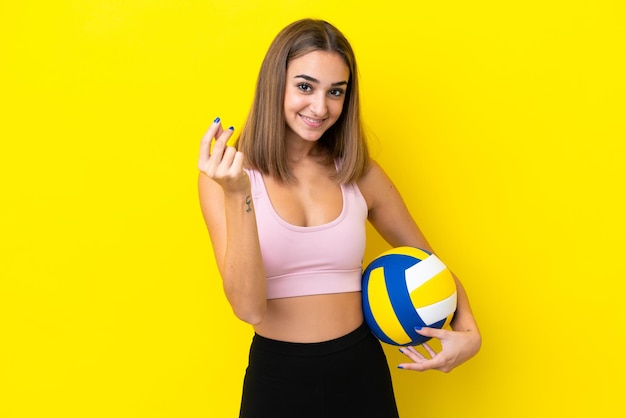 Giovane donna che gioca a pallavolo isolata su fondo giallo che fa il gesto dei soldi