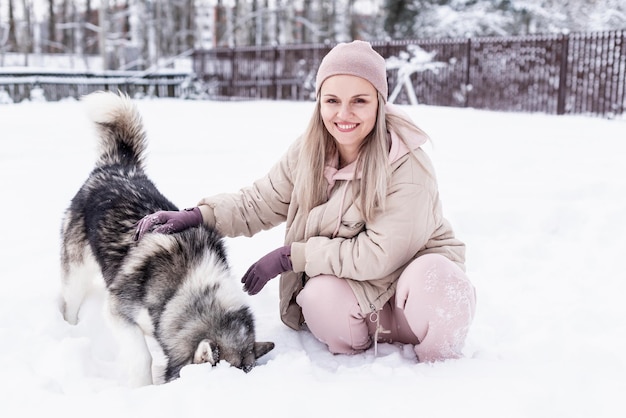 Giovane donna che gioca con il cane husky siberiano nella neve in una giornata invernale, addestrando e portando a spasso il suo cane. Amicizia, cane adorabile, miglior animale domestico, cane per una passeggiata con il suo proprietario