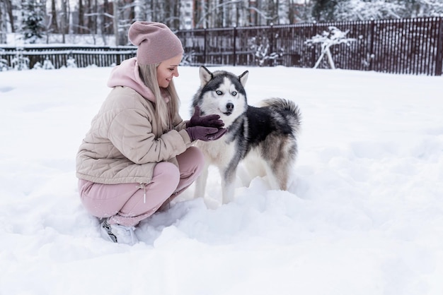 Giovane donna che gioca con il cane husky siberiano nella neve in una giornata invernale, addestrando e portando a spasso il suo cane. Amicizia, cane adorabile, miglior animale domestico, cane per una passeggiata con il suo proprietario