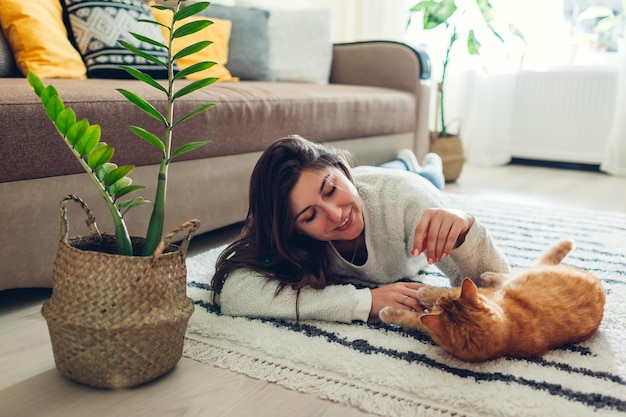 Giovane donna che gioca con il gatto sul tappeto a casa maestro sdraiato sul pavimento con il suo animale domestico