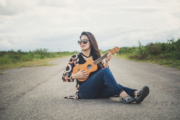 Giovane donna che gioca su Ukulele marrone nel parco.