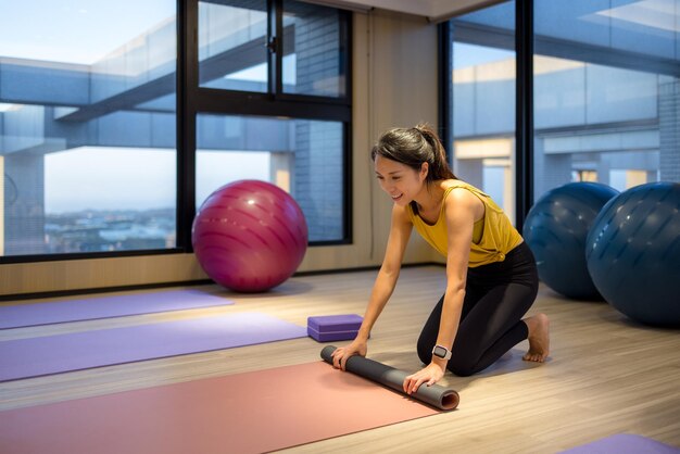 Giovane donna che gira il tappetino da yoga dopo l'allenamento sportivo