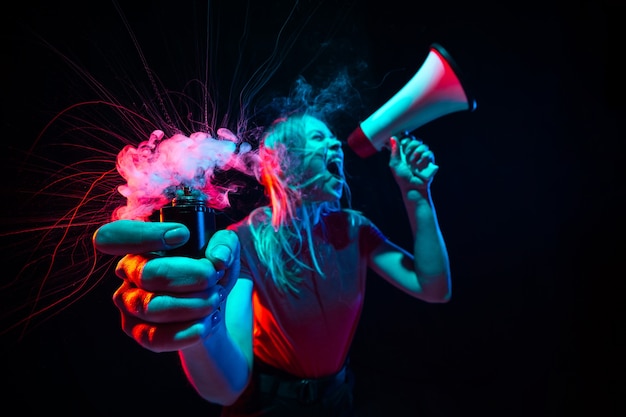 Giovane donna che grida con megafono e fumo in luce al neon su sfondo nero
