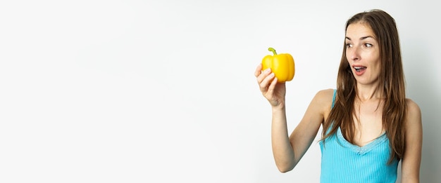 Giovane donna che guarda con sorpresa la paprika gialla isolata su sfondo bianco Banner