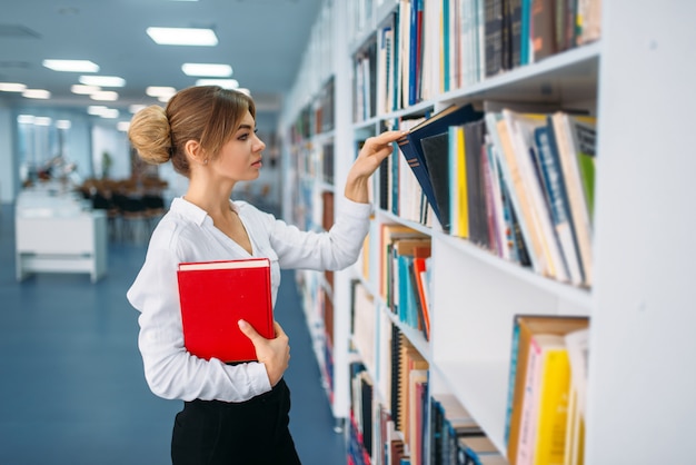 Giovane donna che guarda il libro allo scaffale in libreria. Persona di sesso femminile in sala di lettura, deposito di conoscenze