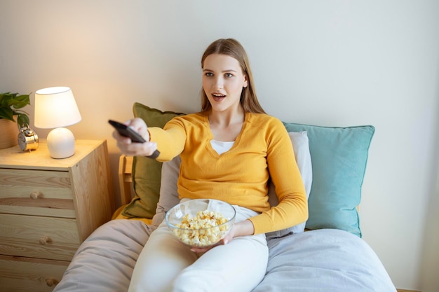 Giovane donna che guarda la televisione godendosi i programmi televisivi preferiti in camera da letto