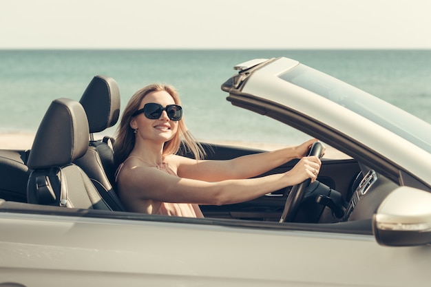 Giovane donna che guida un'auto sulla spiaggia