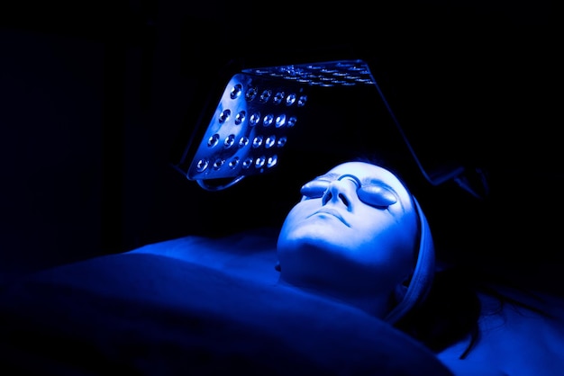 Giovane donna che ha un trattamento di terapia facciale con luce LED blu nel salone di bellezza