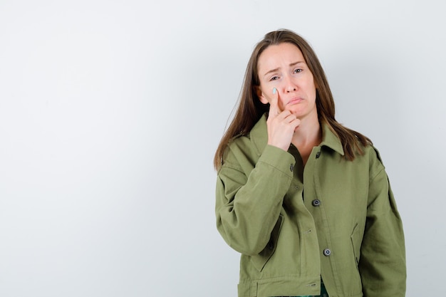 Giovane donna che indica le sue lacrime in giacca verde e sembra depressa, vista frontale.