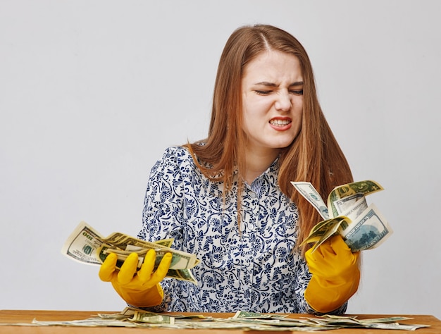 Giovane donna che indossa guanti di gomma gialli e guardando le banconote da un dollaro con disgusto