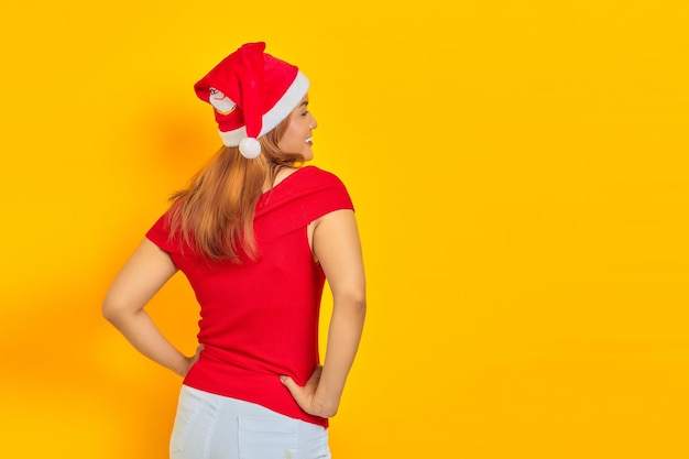 Giovane donna che indossa il cappello di Natale in posizione posteriore tenendo le mani sulla vita con fiducia