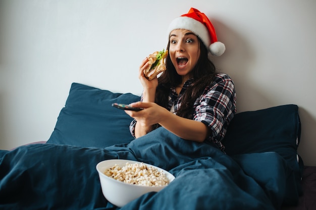 Giovane donna che indossa il cappello di Natale mangiare a letto